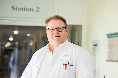 Chefarzt Chirurgie Alwin Bulla, Mann mit wei&szlig;em &Auml;rztekittel im Krankenhausflur.