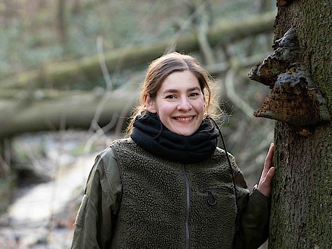 Autorin Farina Gra&szlig;mann im Wald an einen Baum gelehnt.