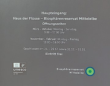 Eingangst&uuml;r des Infozentrums Haus der Fl&uuml;sse mit aufgedruckten &Ouml;ffnungszeiten sowie Logo.